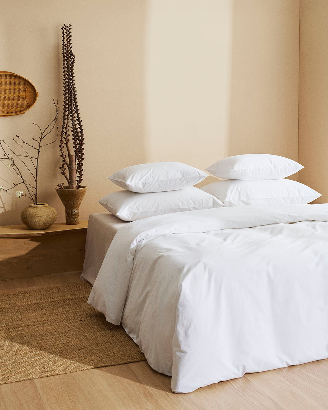 Neatly made bed with white bedding in a room with a wooden floor and beige walls.