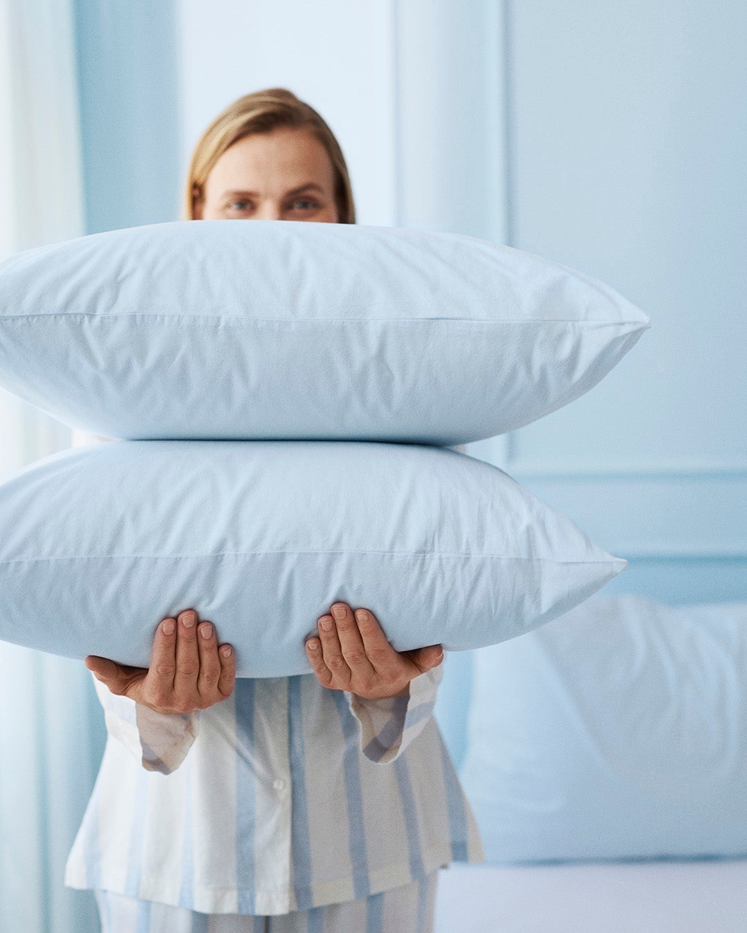 Person holding two pillows in front of a light blue curtain